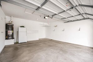 A spacious, empty room with a concrete floor, a white refrigerator, a water heater, and a ceiling with exposed metal beams. - Pet-Friendly 3BR | Fenced Yard | King Bed (Chandler)