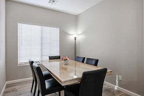 Un comedor con una mesa rectangular, seis sillas, una lámpara de pie y un ventanal con persianas.