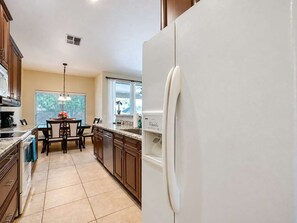 Una cocina con refrigerador, armarios, una mesa de comedor con sillas y una ventana con persianas.