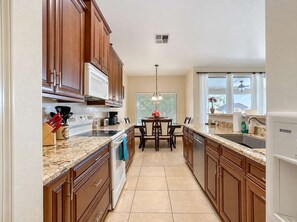 A kitchen with wooden cabinets, a granite countertop, a built-in oven, and a dining area with a table and chairs. - Pet-Friendly 4BR | Fenced Yard | King Bed (Chandler)