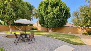 A patio with a table and chairs, surrounded by a well-maintained lawn and trees.