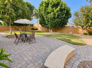 A patio with a table and chairs, surrounded by a well-maintained lawn and trees.