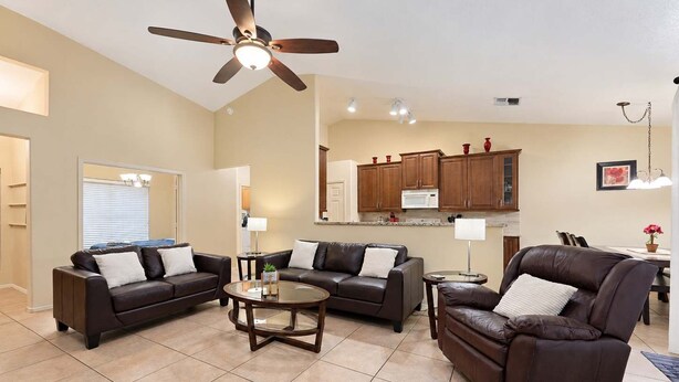 A spacious living room with a ceiling fan, a dining area with a table and chairs, and a kitchen with wooden cabinets and a microwave.