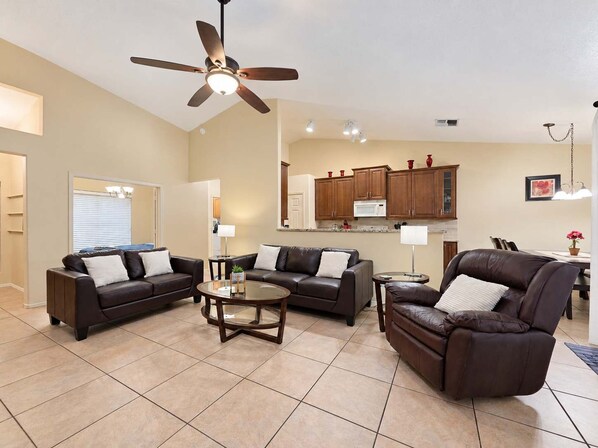 A spacious living room with a ceiling fan, a dining area with a table and chairs, and a kitchen with wooden cabinets and a microwave.