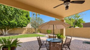 A patio with a table and chairs, a ceiling fan, and a large umbrella.