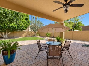 A patio with a table and chairs, a ceiling fan, and a large umbrella.