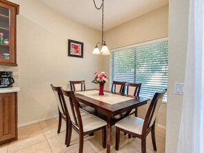 A dining area with a wooden table, six chairs, a vase with flowers, a coffee maker, and a framed picture on the wall. - Pet-Friendly 4BR | Fenced Yard | King Bed (Chandler)