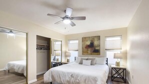 A bedroom with a large bed, a ceiling fan, a mirror, and a painting on the wall. - Immaculate!  Single-Story 3bdr | Chandler (Chandler)