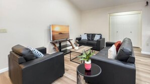A modern living room with a flat-screen TV, two black sofas, a coffee table, and a small plant. - Immaculate!  Single-Story 3bdr | Chandler (Chandler)