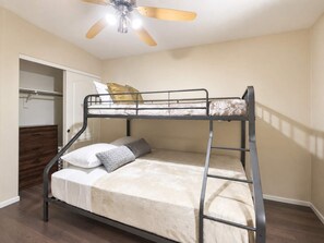 Un lit superposé avec un ventilateur de plafond, une commode en bois et un placard.