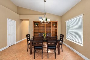 A dining area with a table and chairs, a chandelier, a bookshelf, and a window with blinds. - Pet-Friendly 3BR | Fenced Yard | Lake Trails (Tempe)