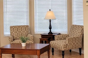 A room with two patterned armchairs, a wooden coffee table, a floor lamp, and a potted plant.