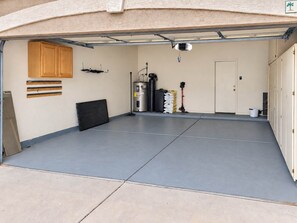 A clean, empty garage with a concrete floor, a wooden cabinet, and a door with a palm tree sign. - Pet-Friendly 3BR | Fenced Yard | Lake Trails (Tempe)