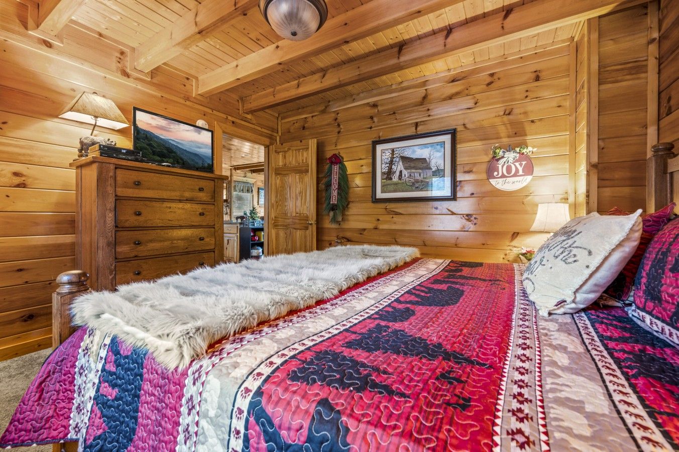 Een slaapkamer in een houten chalet met een bed, een dressoir, een televisietoestel en een lijst aan de muur.
