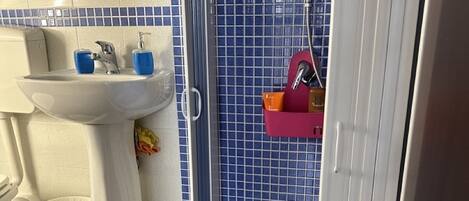 A bathroom with a white sink, blue-tiled shower, and a white towel on the floor.