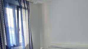 Una cama bien hecha con ropa de cama azul y almohadas blancas, una mesita de noche con una lámpara y una ventana con cortinas azules.