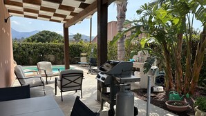 Un patio exterior con una parrilla, sillones de descanso y una piscina.