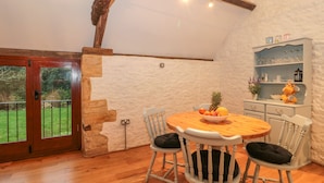 Un coin repas chaleureux avec une table et des chaises en bois, un panier de fruits et un mur en pierre.