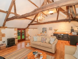 A cozy living room with a stone wall, wooden beams, a sofa, a coffee table, and a fireplace.