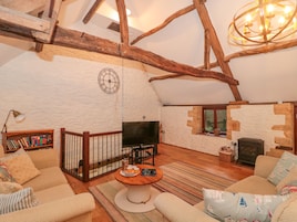 A cozy loft-style living room with exposed wooden beams, a fireplace, a television, and a bookshelf.