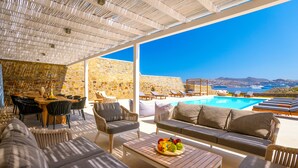Ett soligt utomhusområde med en lounge, en pool, stenmurar och utsikt över havet.