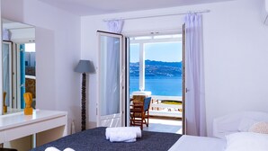 Ett hotellrum med en säng, ett skrivbord, en stol och utsikt över havet.