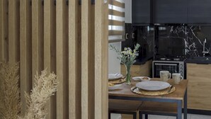A modern kitchen with a built-in oven, a coffee machine, and a dining area with a wooden table and chairs.