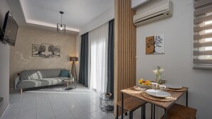A modern living room with a sofa, a dining table with plates and a vase, and an air conditioning unit on the wall.