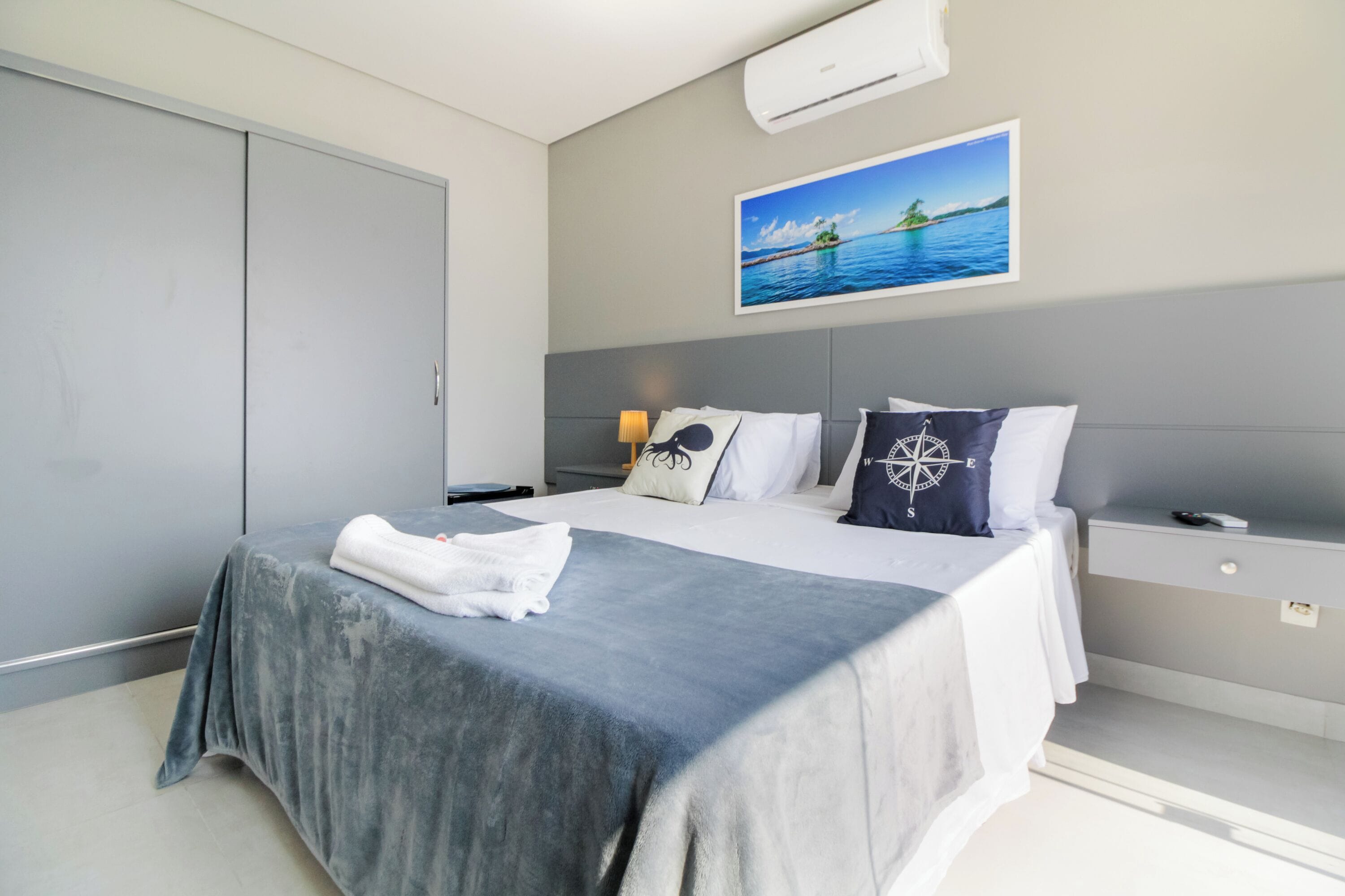 Una habitación de hotel moderna con una cama grande, una mesita de noche, un escritorio y un cuadro con una escena costera.