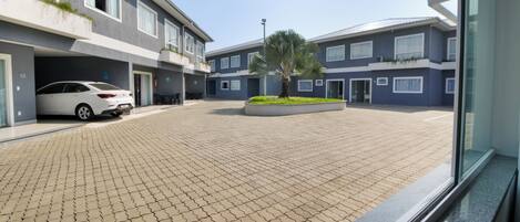 A modern building with a paved courtyard, a white car parked in a covered area, and a palm tree in the center.