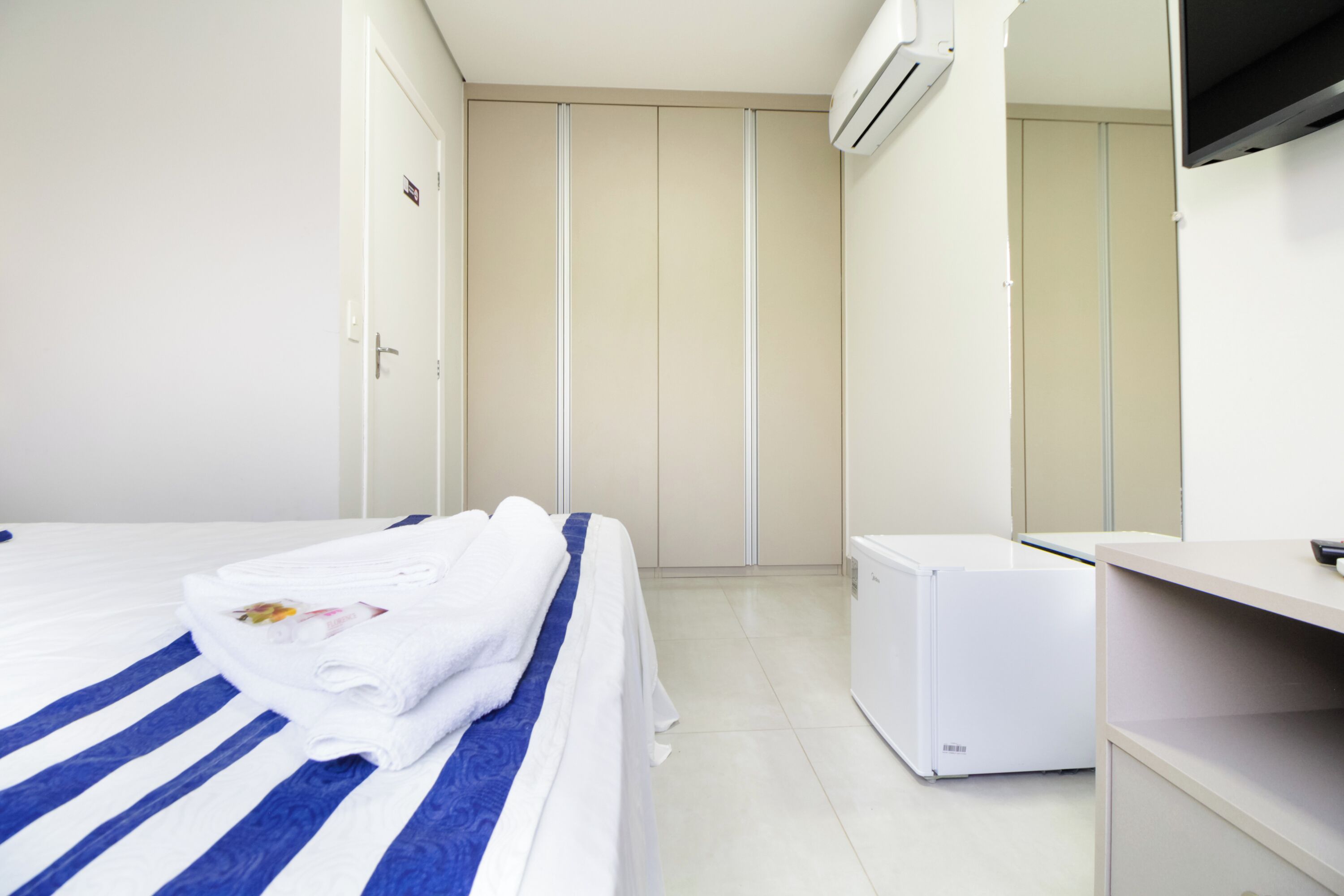 Una habitación de hotel con una cama, un refrigerador blanco pequeño y un armario.