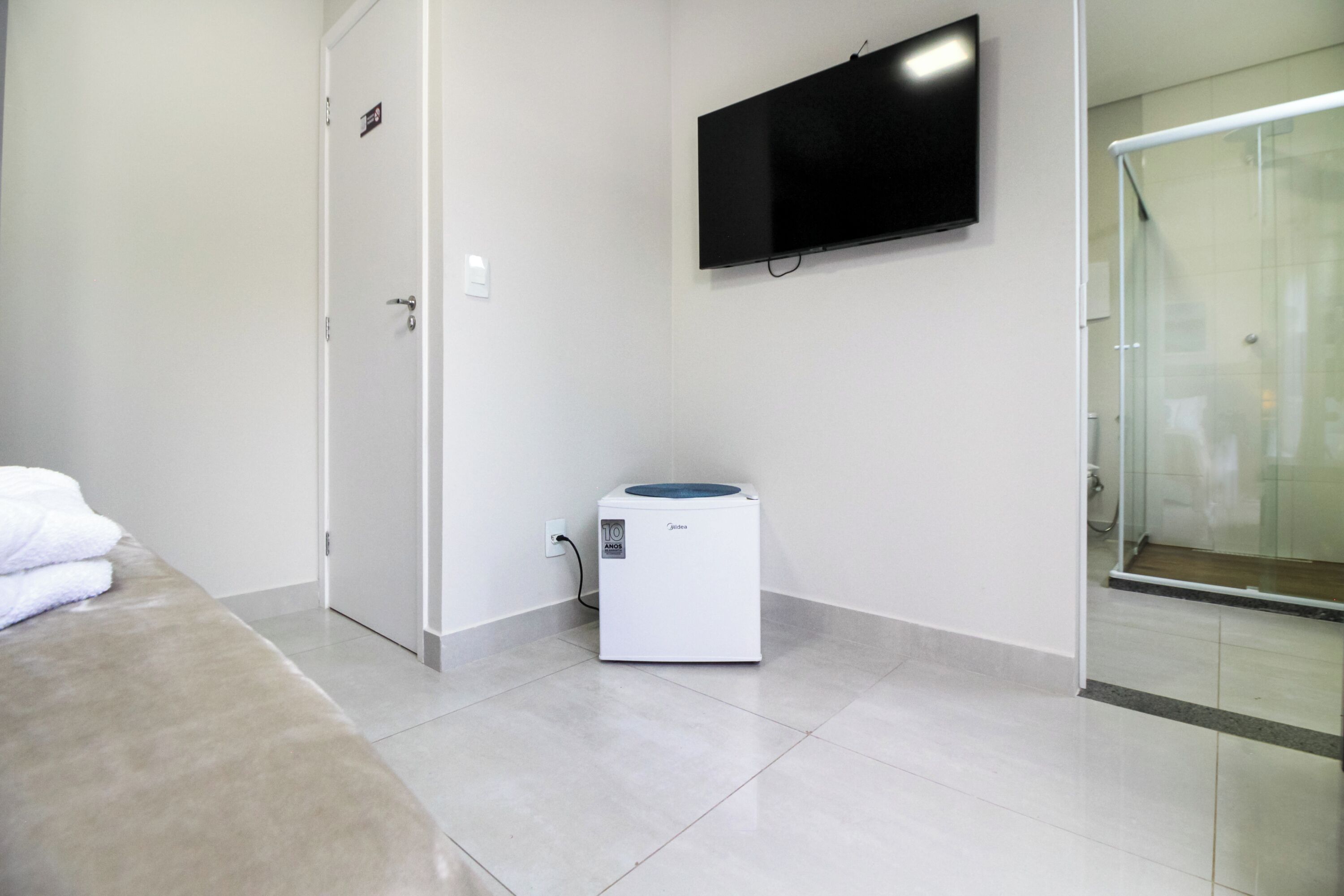 A hotel room with a bed, a washing machine, a television, and a shower area.
