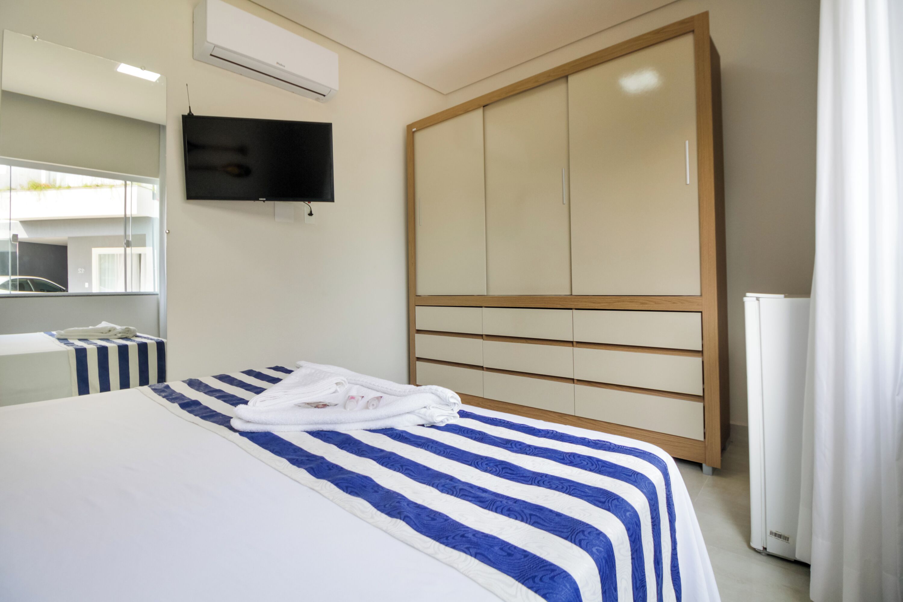 A hotel room with a bed, a TV, a wardrobe, and a window.