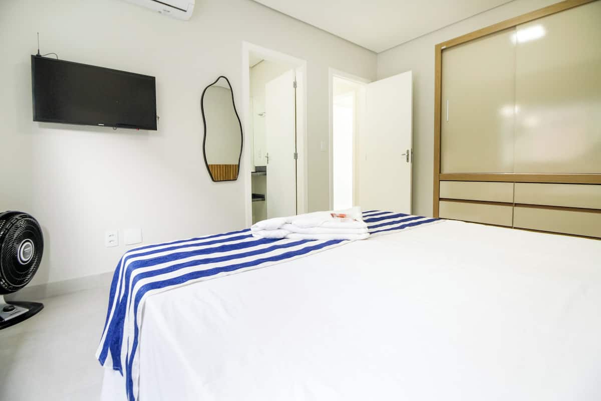 A hotel room with a bed, a fan, a TV, a mirror, and a wardrobe.