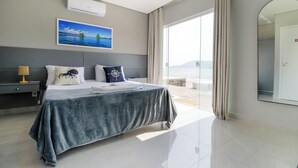 A modern hotel room with a large bed, a view of the sea, and a large mirror.