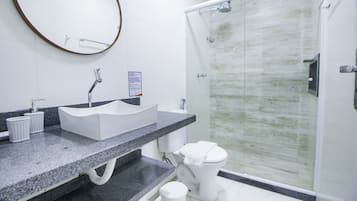 A modern bathroom with a granite countertop, a white sink, and a glass shower enclosure.