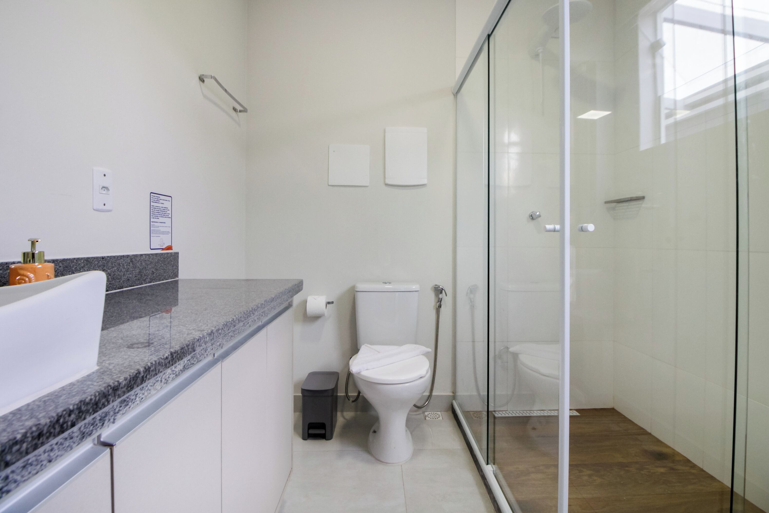 A modern bathroom with a glass shower enclosure, a white toilet, and a granite countertop.
