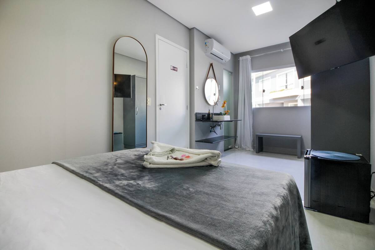 A modern hotel room with a bed, a bathroom, a TV, and a view of the outside.