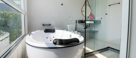 A modern bathroom with a large bathtub, a glass shower enclosure, and a view of greenery outside.