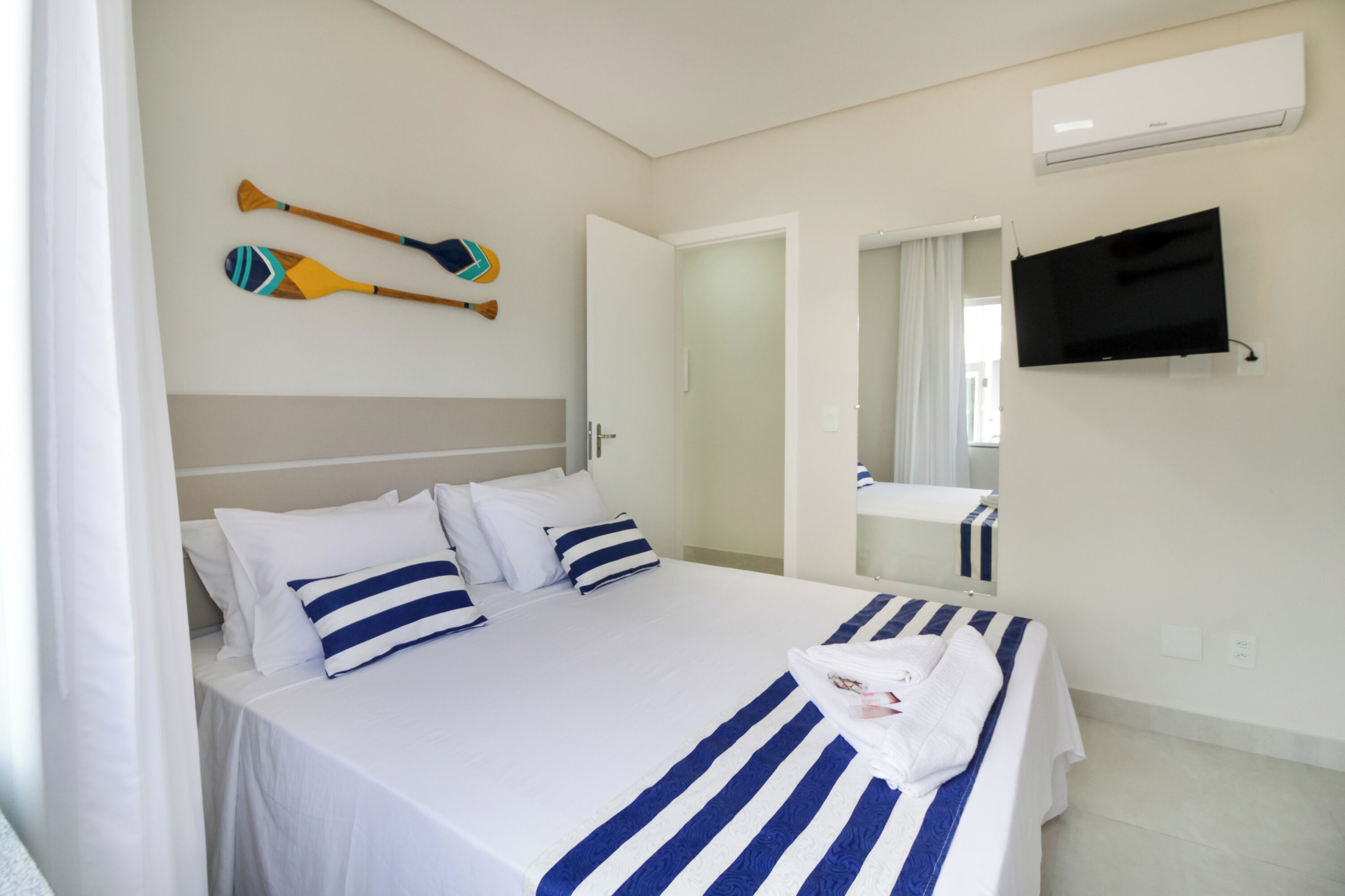A hotel room with a bed, a television mounted on the wall, and a mirror above the sink.