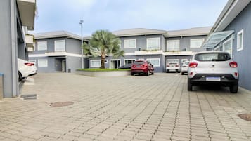 Kerrostalo, jossa on asuintiloja useissa kerroksissa, asfaltoitu ajotie ja parkissa olevia autoja.