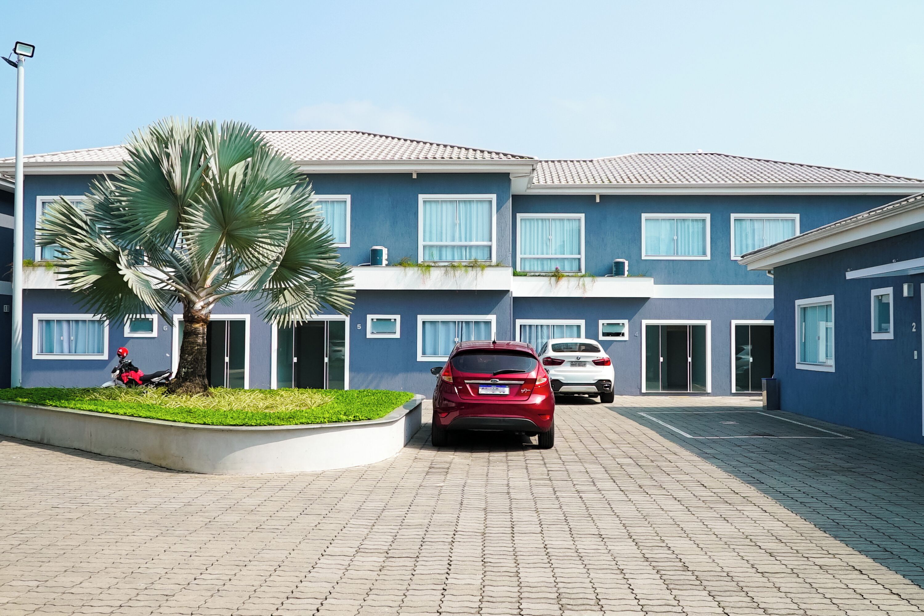 A modern building with a blue facade, a paved driveway, and a parked red car.