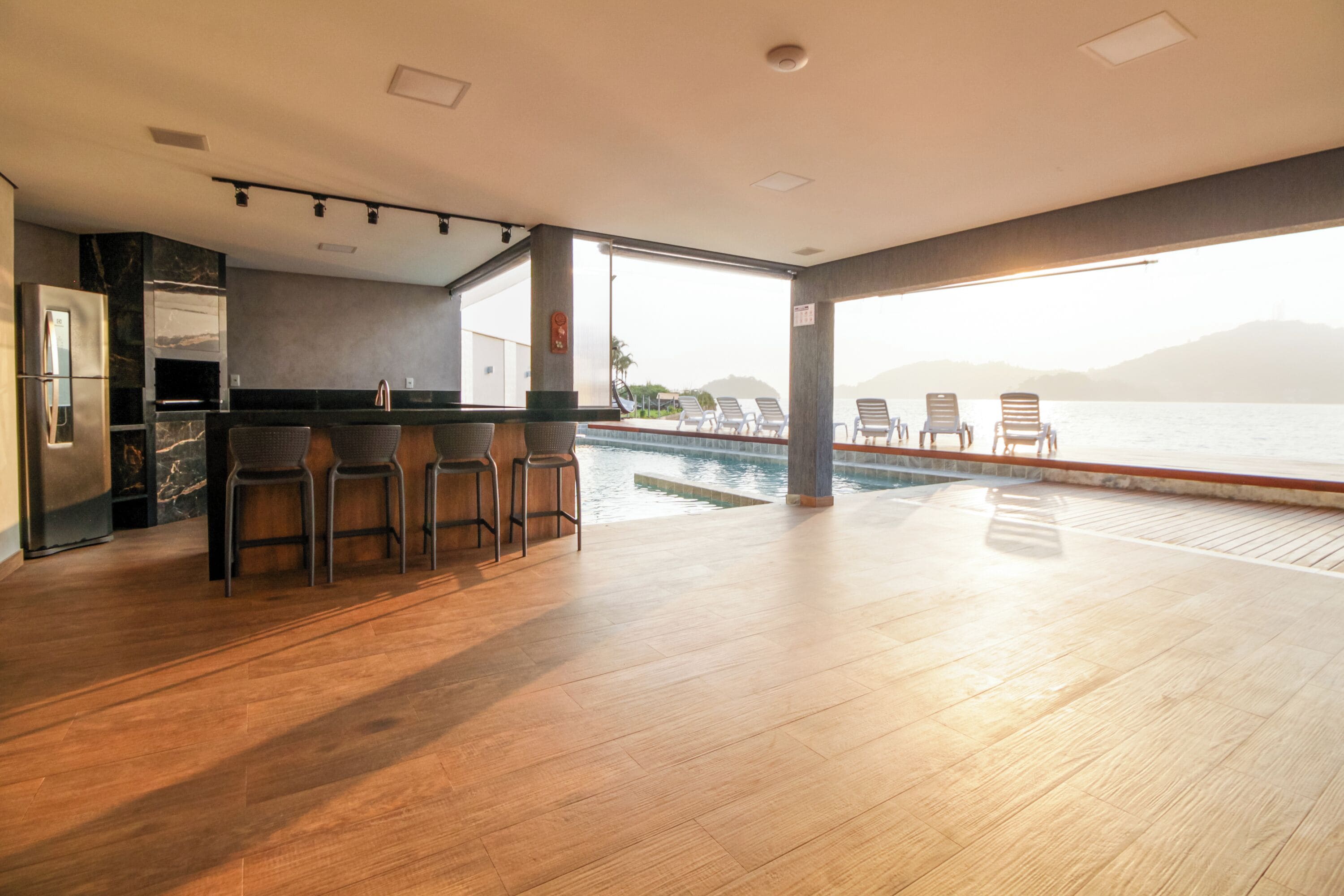 A modern kitchen with a bar area, a poolside lounge, and a view of the sea.