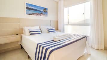 Una camera d'albergo con un letto grande, un comodino, una finestra con tende e un quadro raffigurante una spiaggia.