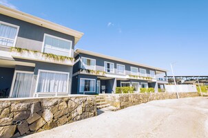 Un moderno edificio residencial de varios pisos con un muro de contención de piedra y cielo despejado.