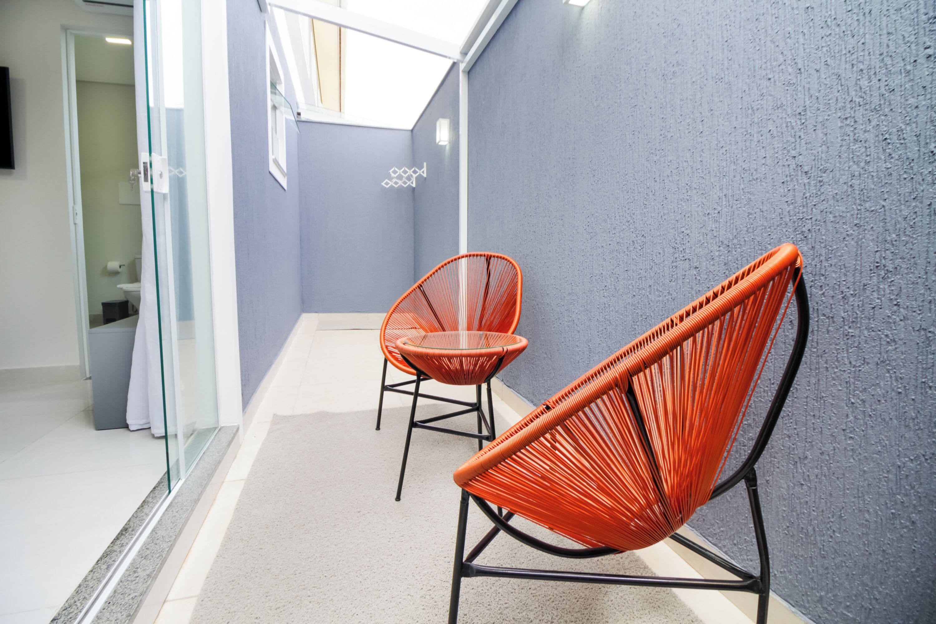 A hallway with two orange wicker chairs, a glass partition, and a blue textured wall.