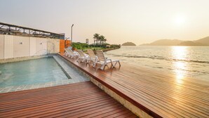 A pool area with lounge chairs and a wooden deck overlooking a body of water.
