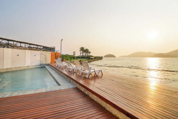 A pool area with lounge chairs and a wooden deck overlooking a body of water. - VELINN Pousada Angra Sunset (Angra dos Reis)