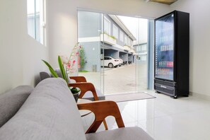 A modern hotel lobby with a seating area, a vending machine, and a view of the parking area. - VELINN Pousada Angra Sunset (Angra dos Reis)