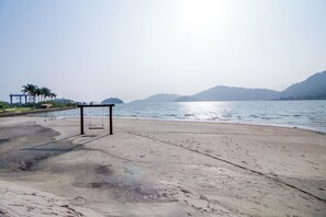 A beach with a swing set and palm trees in the background.